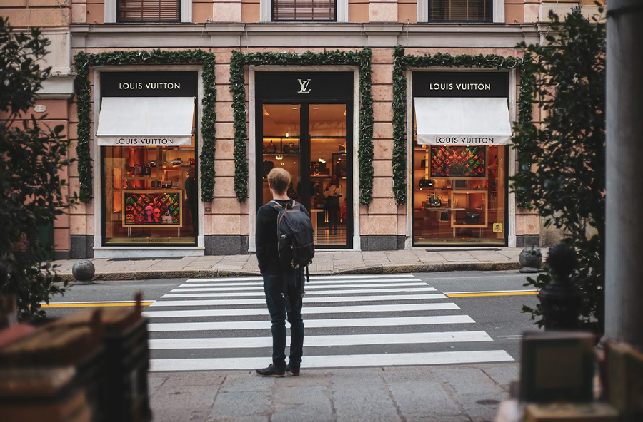 A man stands in front of a Louis Vuitton store.
