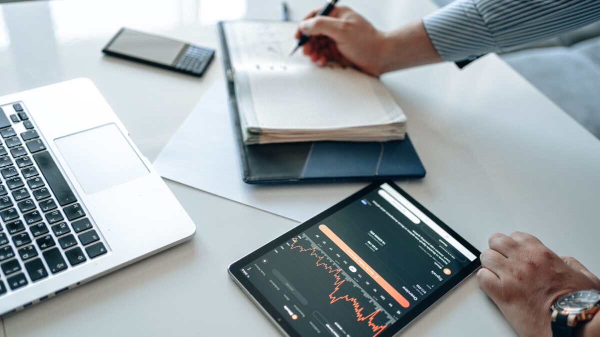 An image showing a person taking notes in a notepad, with a tab showing a graph of trends.