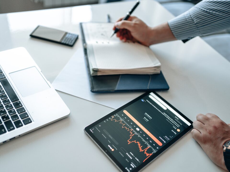 An image showing a person taking notes in a notepad, with a tab showing a graph of trends.