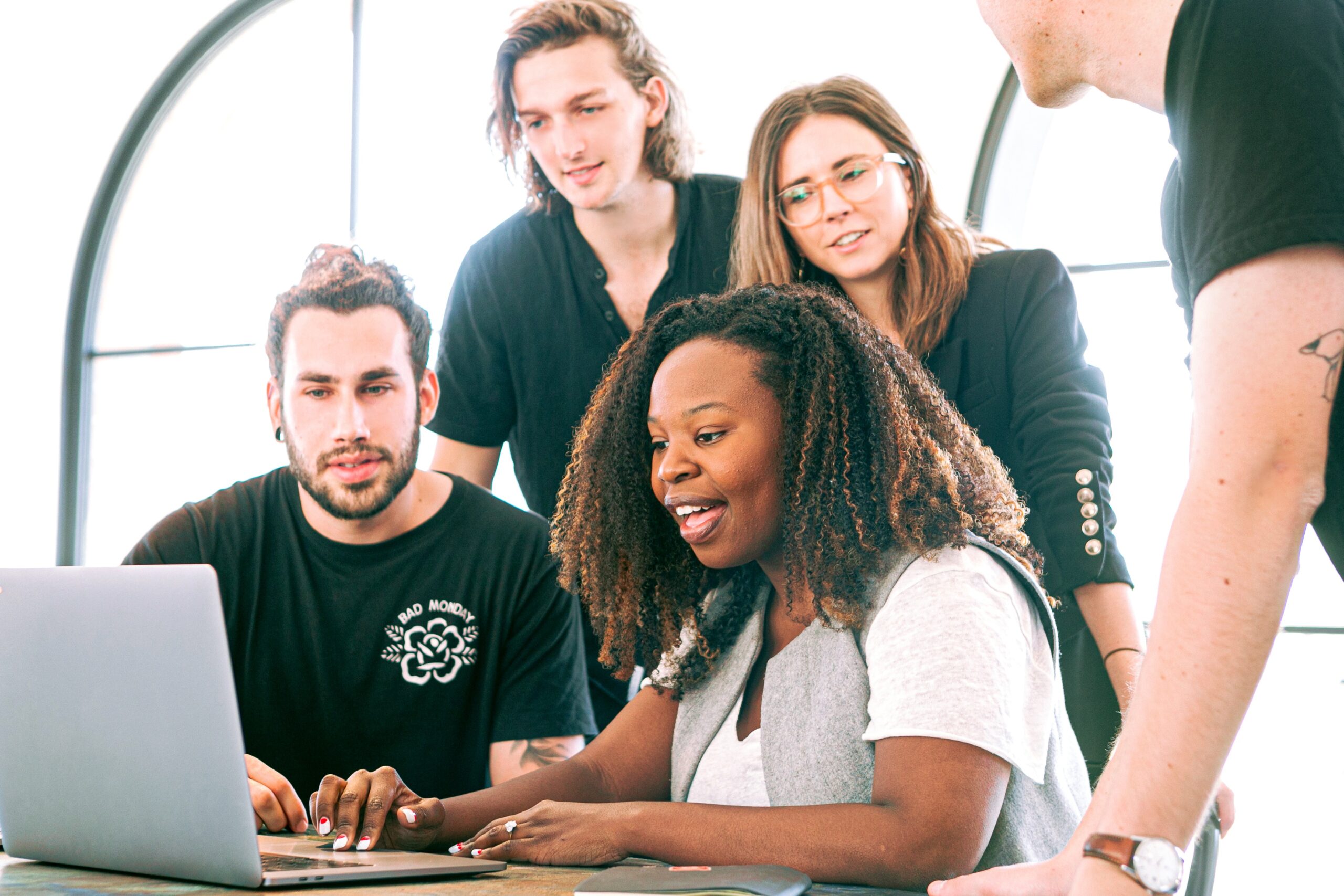 A woman shows something on the laptop, and three men and one woman look at the screen